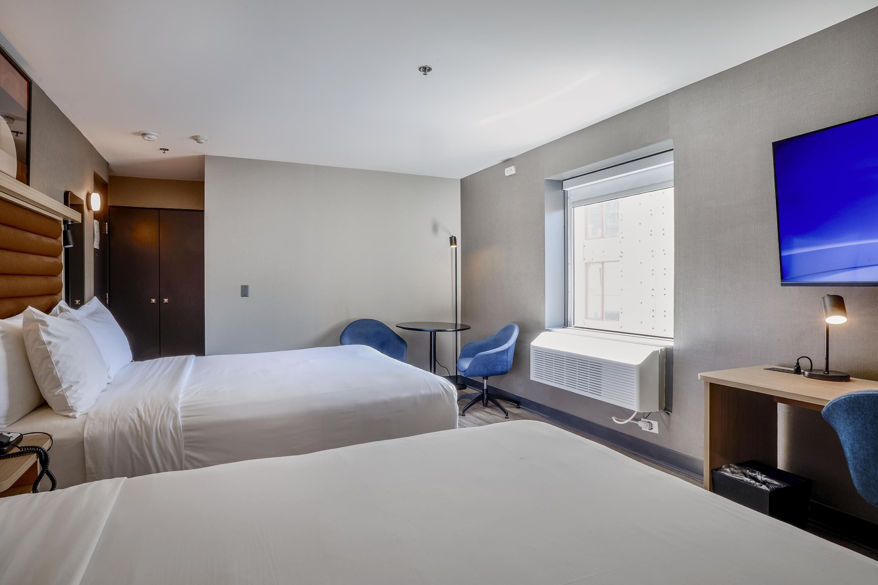 Habitación de hotel con dos camas, un escritorio, una silla, un televisor y una ventana con persianas.