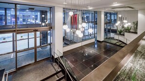 Un moderno vestíbulo de hotel con puertas de vidrio, una escalera y lámparas colgantes.
