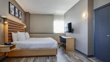 Una habitación de hotel con cama, mesita de noche, lámpara, televisor y escritorio.