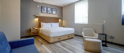 A hotel room with a bed, a blue sofa, a chair, and a window with curtains.