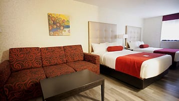 Une chambre d’hôtel avec un canapé à motifs, un lit avec une literie rouge, une table de chevet et un tableau au mur.
