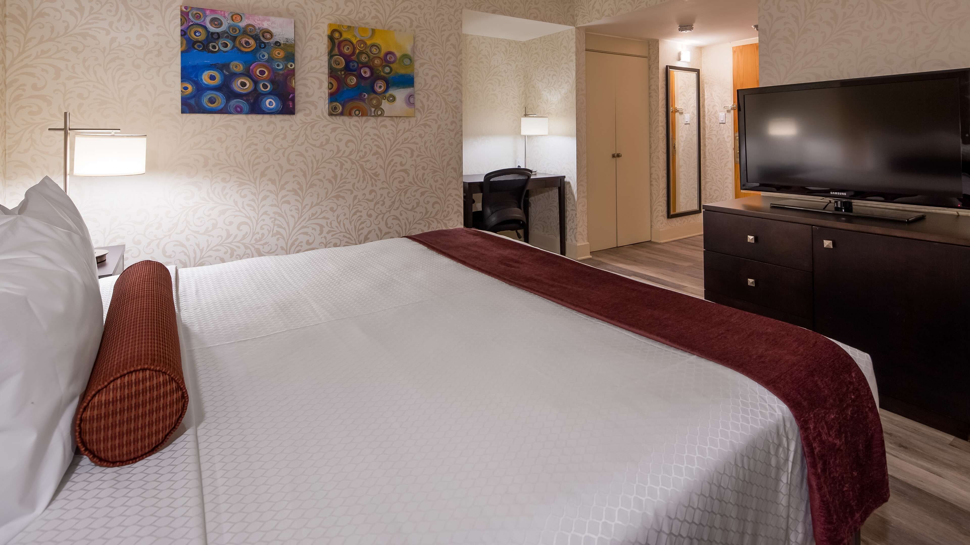 A hotel room with a bed, a desk with a chair, a television, and two paintings on the wall.
