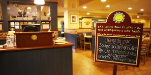Interior d'un restaurant amb un menú escrit a la pissarra que inclou plats com sopa, quiche i formatge.