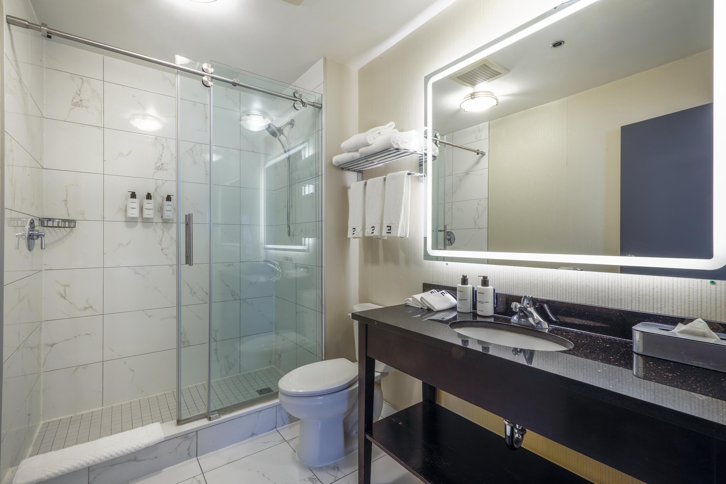 Un baño moderno con cabina de ducha de vidrio, inodoro y tocador con espejo.