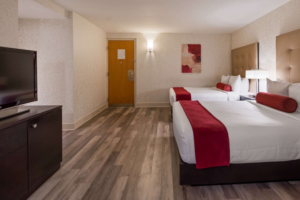 A hotel room with two beds, a TV, and a wooden floor.