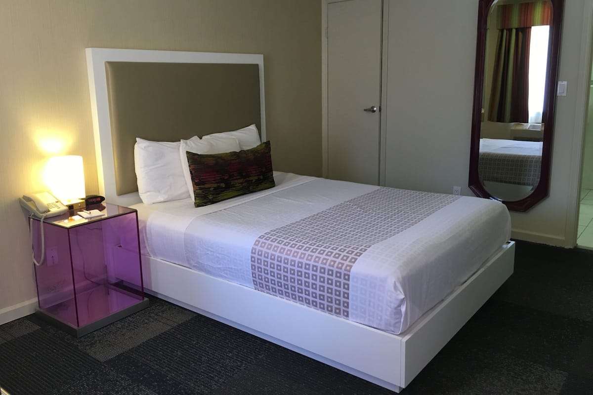 A hotel room with a bed, a bedside table with a lamp, a telephone, and a mirror.