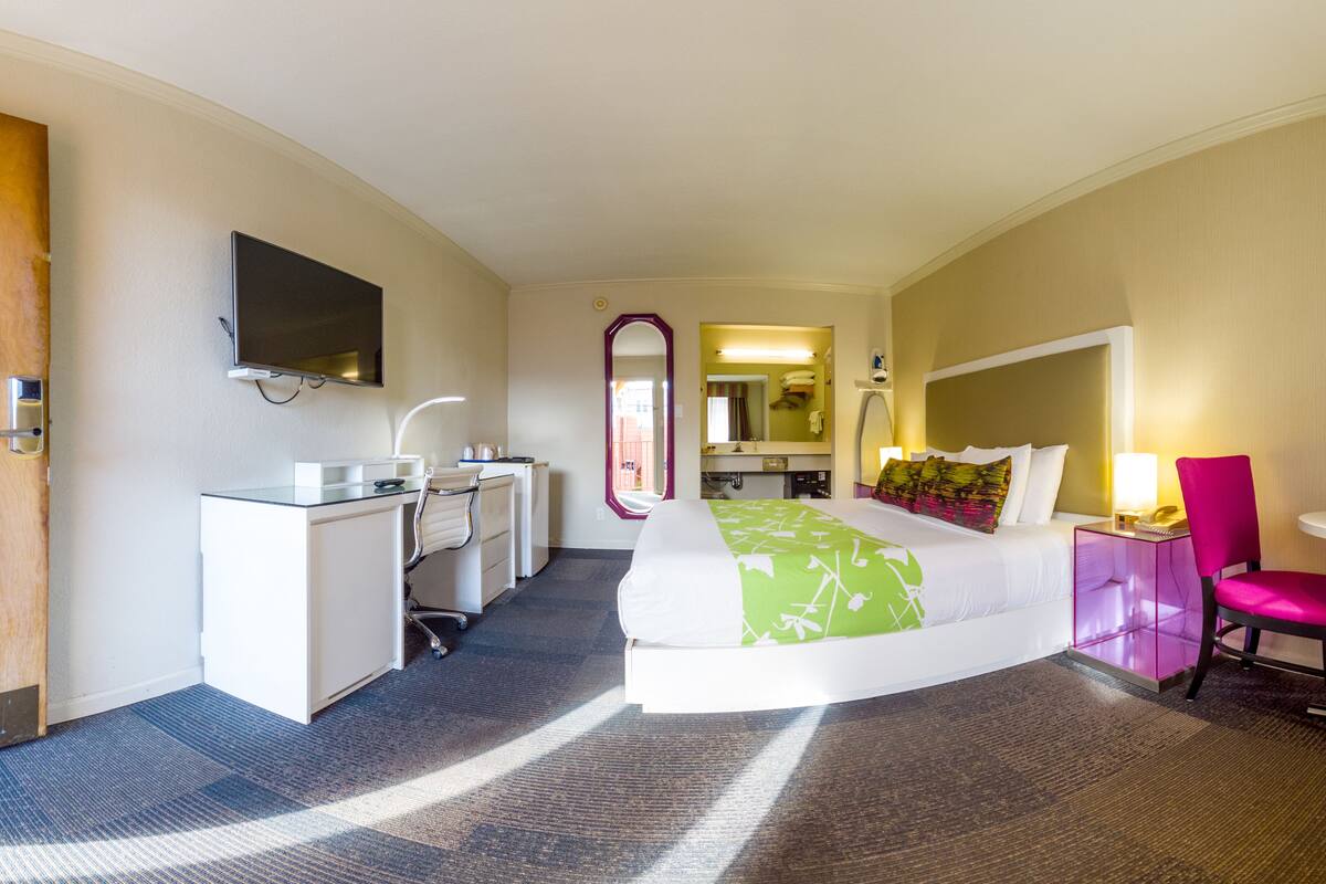 A hotel room with a bed, a desk, a chair, a TV, and a mirror.
