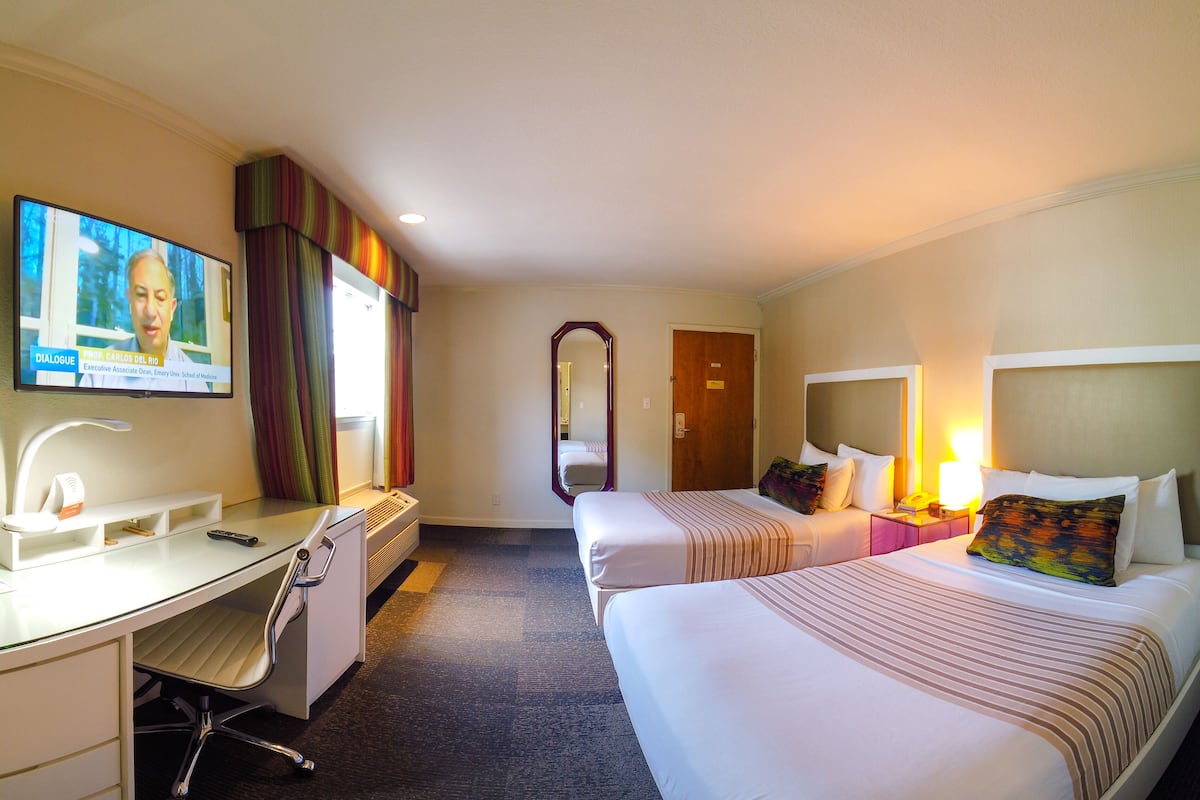 A hotel room with a desk, two beds, a TV, and a mirror.