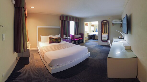 A hotel room with a large bed, a desk, a chair, a mirror, and a television. - Inn at Golden Gate (San Francisco)