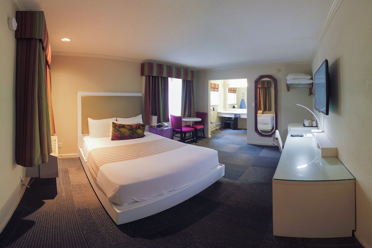 A hotel room with a large bed, a desk, a chair, a mirror, and a television.