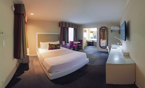 A hotel room with a large bed, a desk, a chair, a mirror, and a television. - Inn at Golden Gate (San Francisco)