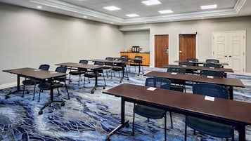 Un salón de conferencias con varias mesas y sillas, una estación de café y dos puertas.