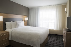Habitación de hotel con una cama grande, cabecera de madera, dos mesitas de noche con lámparas, un televisor y una ventana con cortinas traslúcidas.