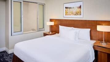 Habitación de hotel con una cama grande, dos mesitas de noche con lámparas, una ventana con vistas y un cuadro enmarcado en la pared.