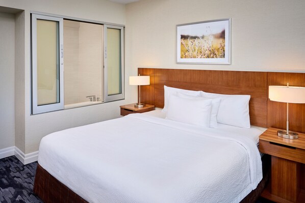 A hotel room with a large bed, two bedside tables with lamps, a window with a view, and a framed picture on the wall.