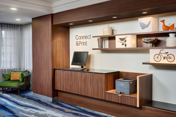 Un mostrador de recepción con computadora, impresora y objetos decorativos en estantes.