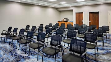 A conference room with rows of black chairs, a podium, and a carpeted floor.