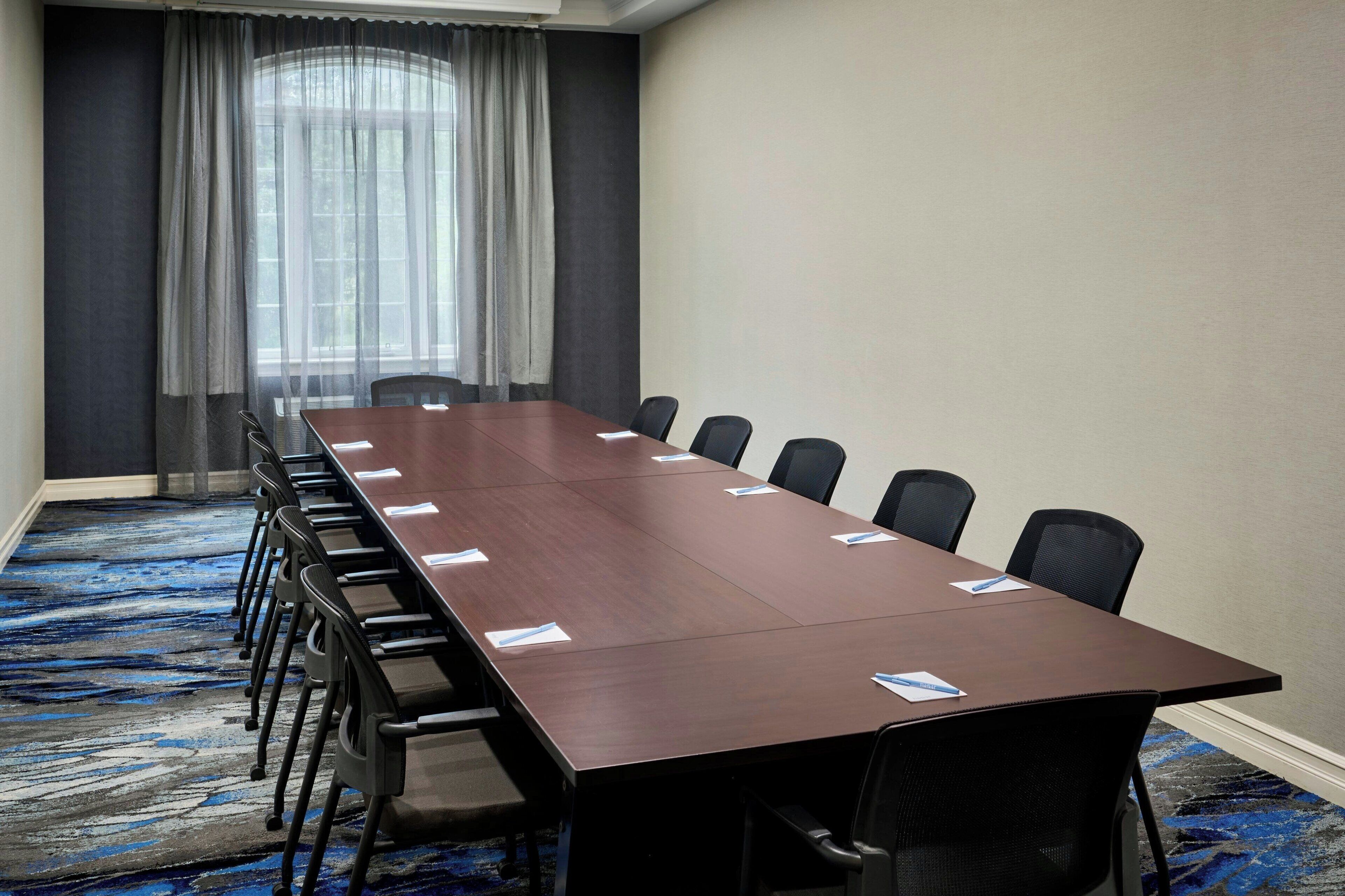 Een vergaderzaal met een lange tafel, zwarte stoelen en een blauw vloerkleed.
