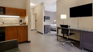 A hotel room with a kitchenette, a bed, a desk with a chair, and a TV.