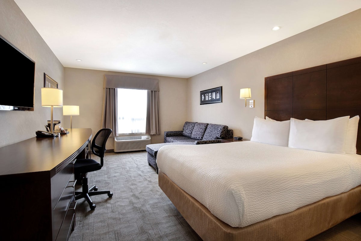 A hotel room with a large bed, a desk with a chair, a sofa, and a television.