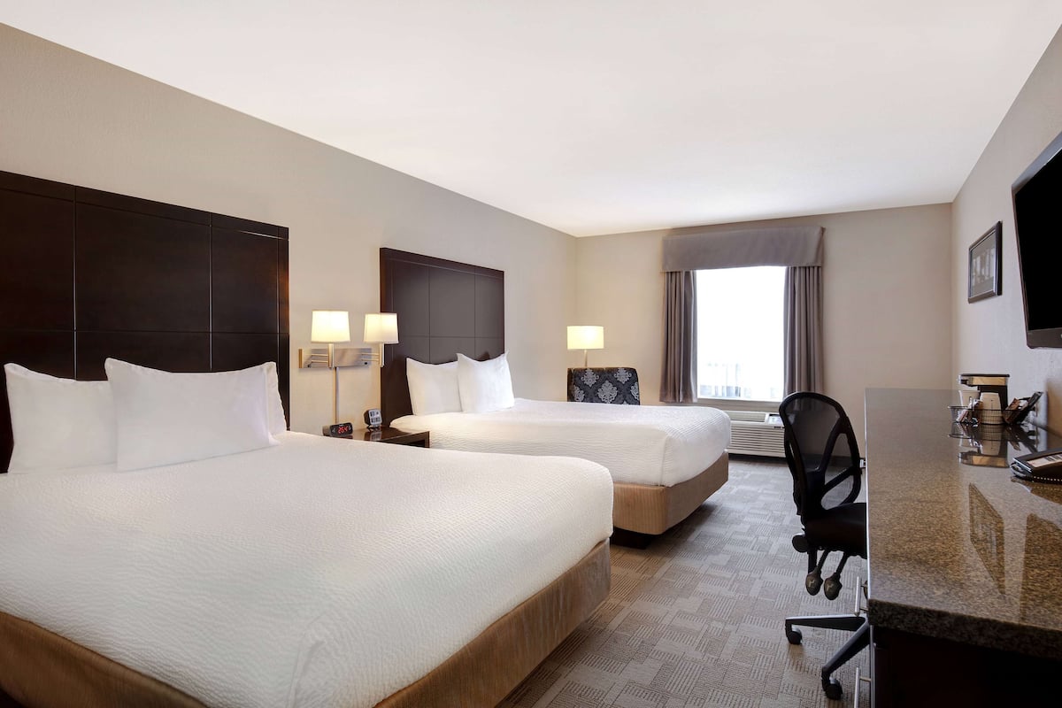 A hotel room with two beds, a desk, a chair, and a television.