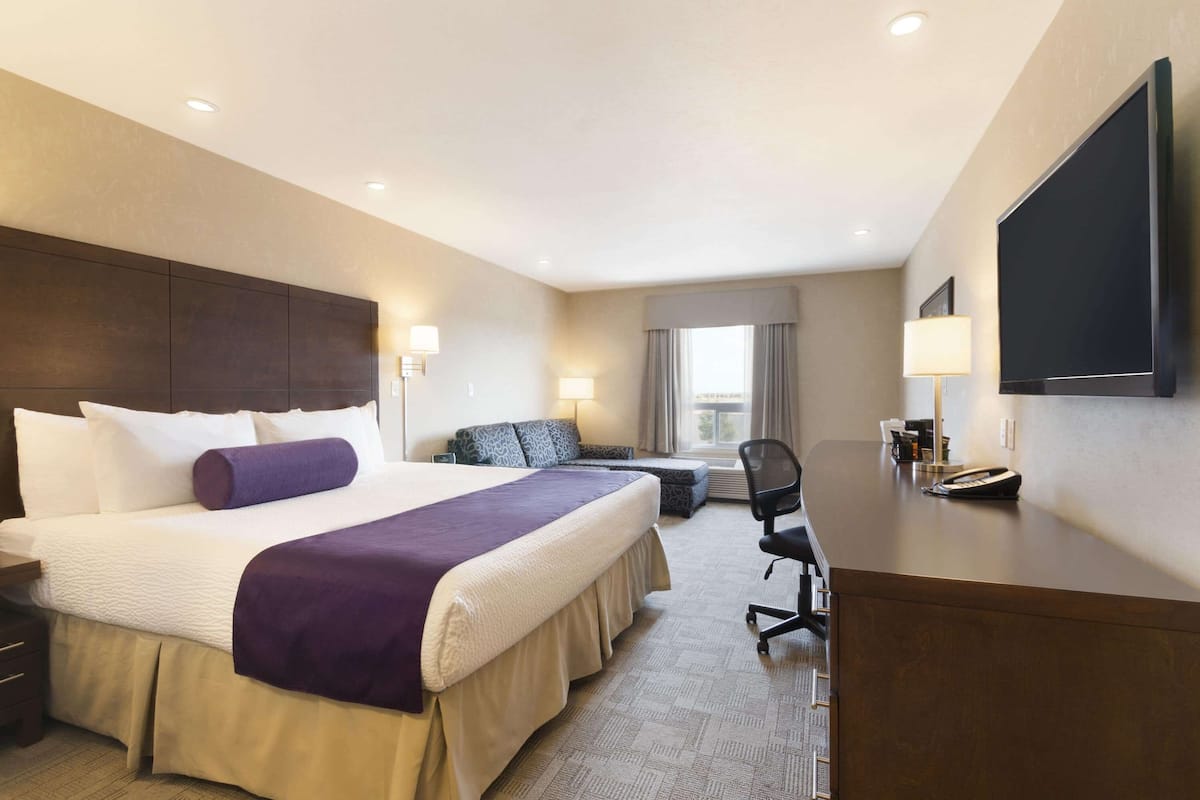 A hotel room with a large bed, a desk, a chair, a TV, and a window with curtains.