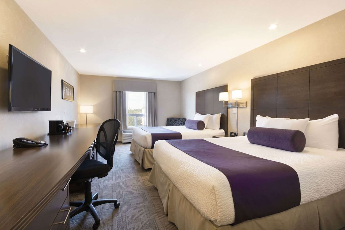 A hotel room with two beds, a desk, a chair, a TV, and a window.