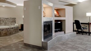 A modern hotel room with a marble bathroom, a fireplace, and a desk with a chair.