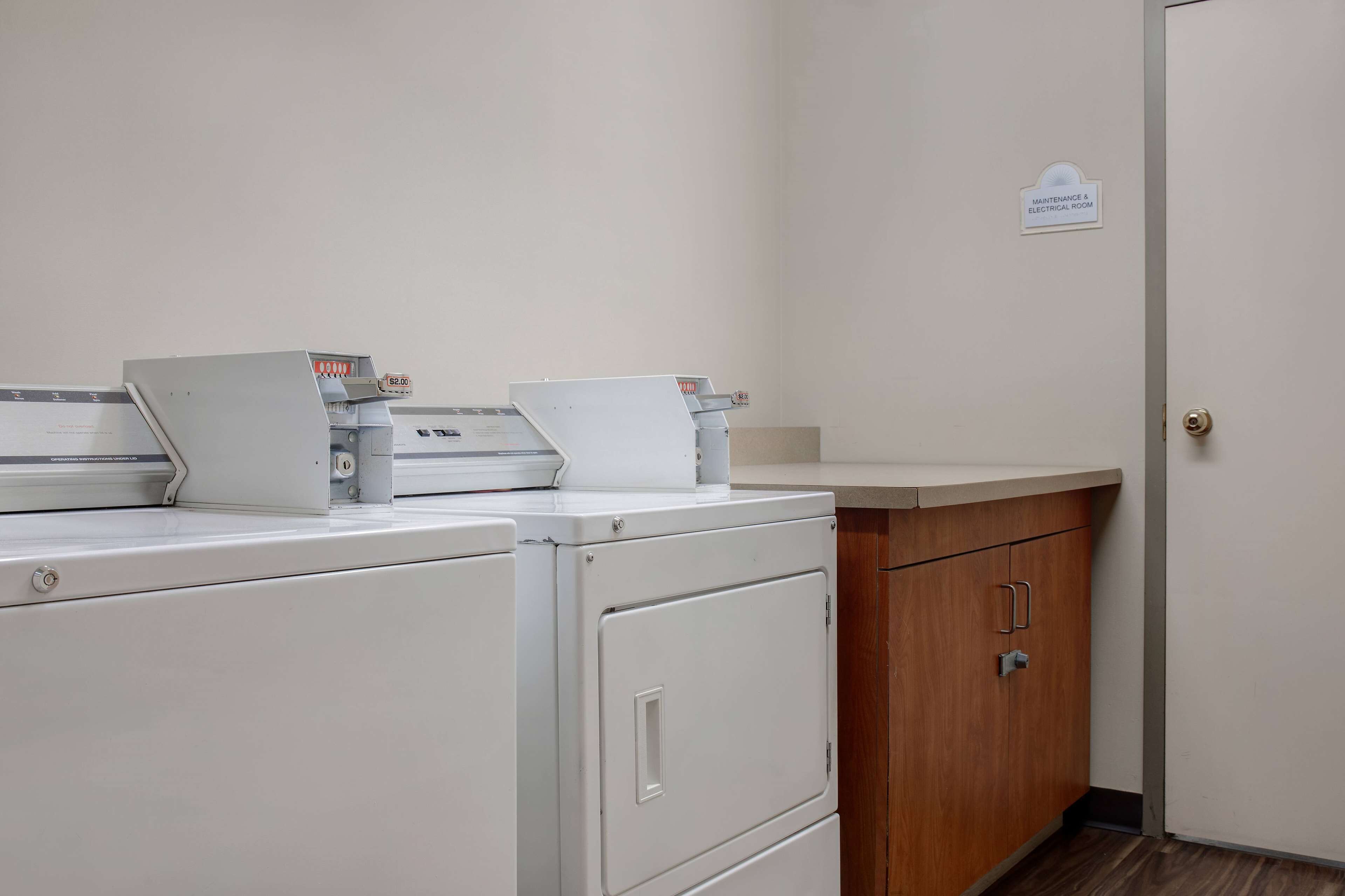 A laundry room with a white washing machine, dryer, and a sign indicating it's a maintenance and electrical room.