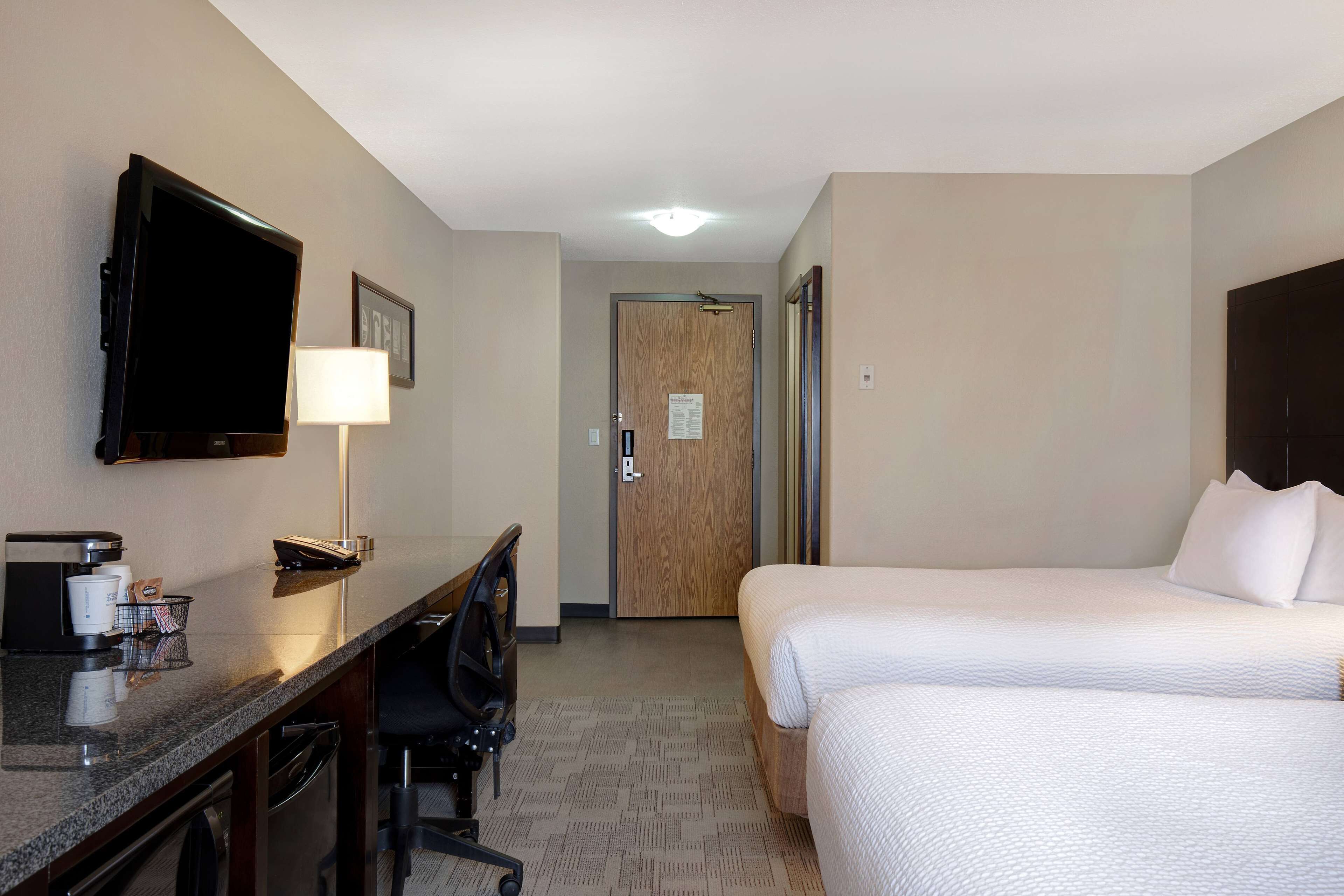 A hotel room with a bed, a desk with a chair, a television, and a lamp.