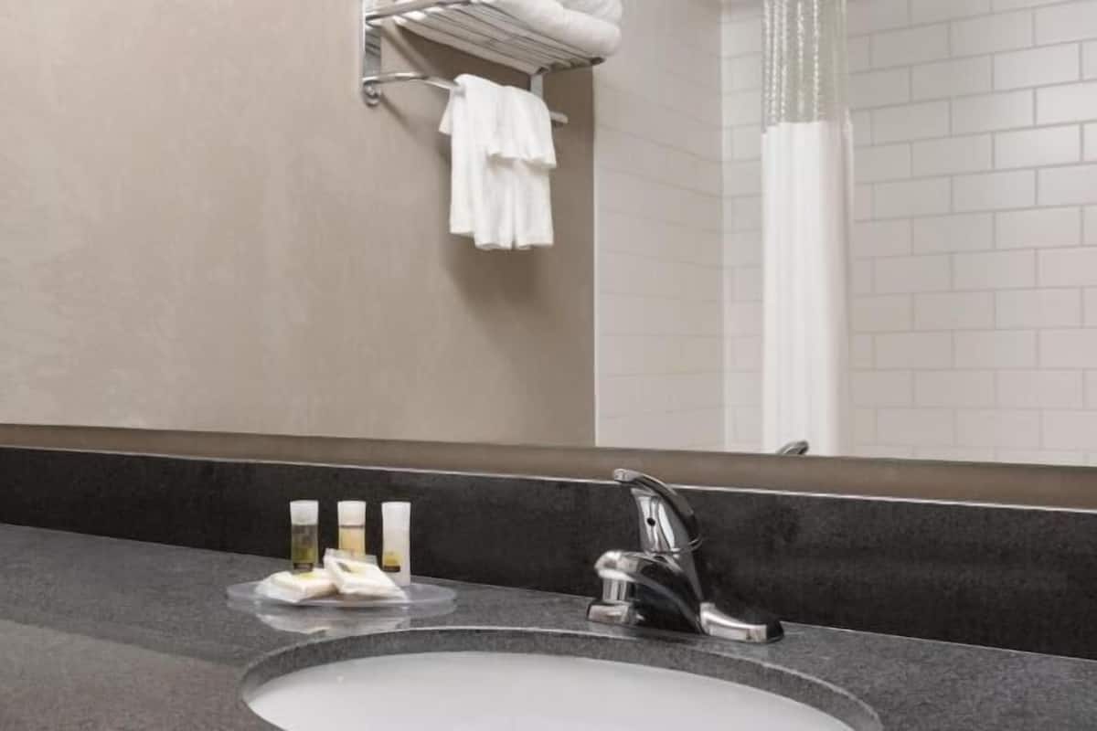 A bathroom with a sink, mirror, towel rack, and toiletries.