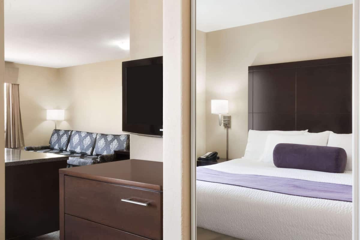 A hotel room with a bed, a desk with drawers, a chair, a television, and a nightstand with a lamp.