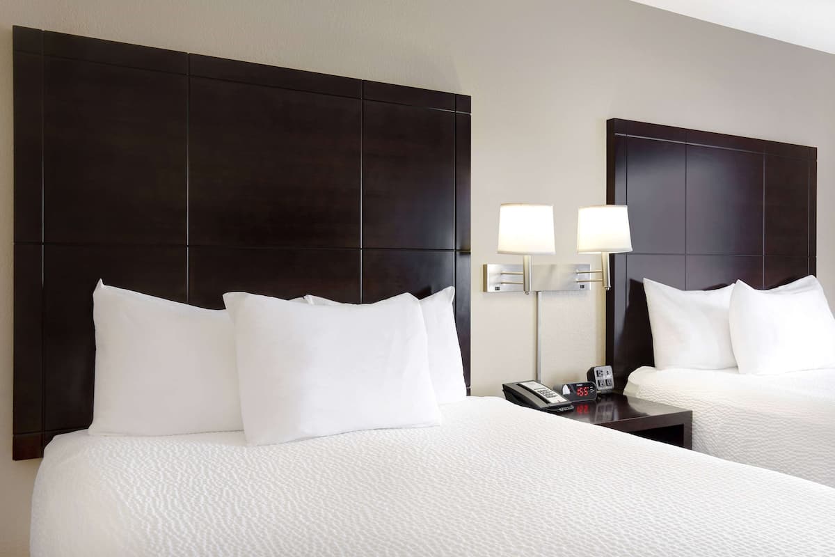 A hotel room with two beds, dark headboards, white bedding, and bedside lamps.