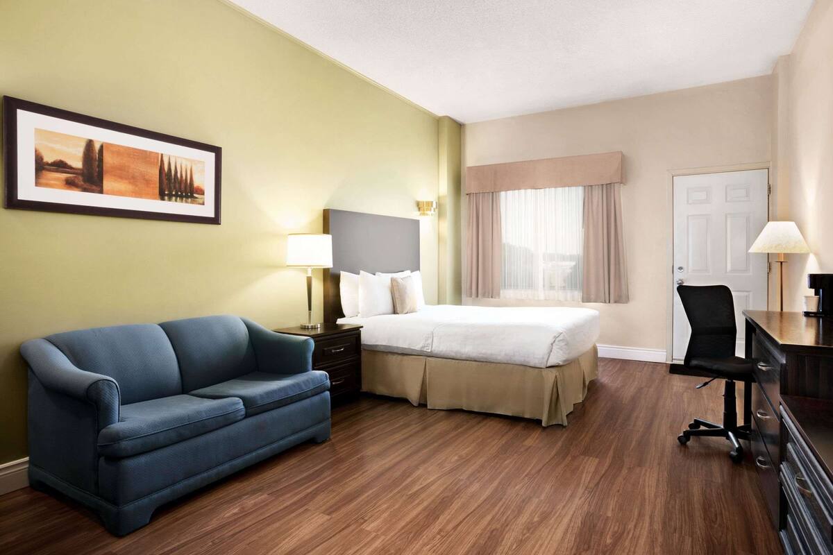 Ein Hotelzimmer mit einem Bett, einem blauen Sofa, einem Schreibtisch mit Stuhl und einem gerahmten Bild an der Wand.