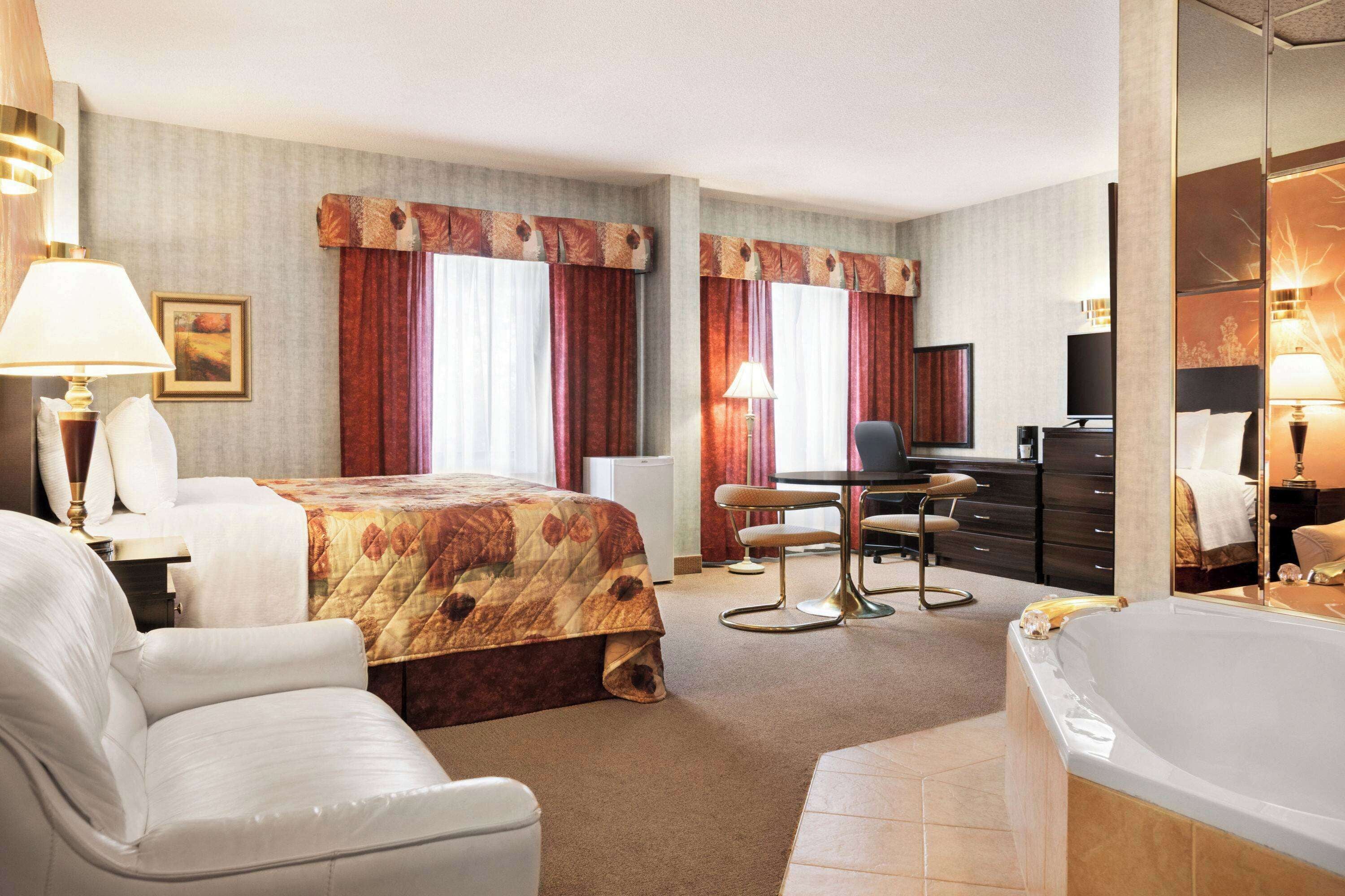 Una habitación de hotel con cama, escritorio, silla, televisor, minibar y bañera.