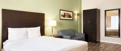 Una habitación de hotel con una cama grande, una lámpara de noche, un sillón a rayas, un armario de madera oscura y un cuadro enmarcado en la pared.