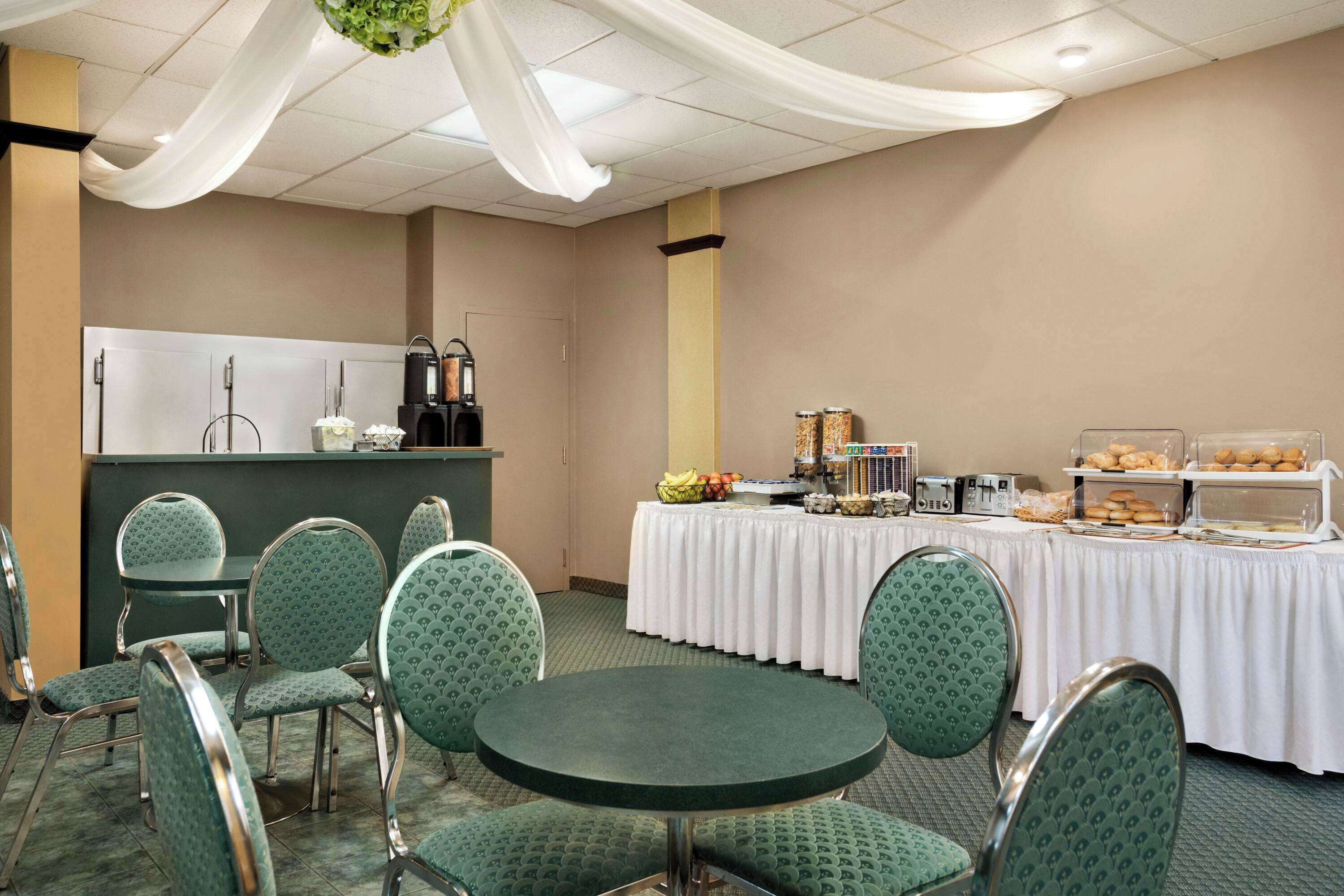 Una sala conferenze con un tavolo per il buffet, sedie imbottite in verde e una tovaglia bianca.