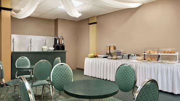 Una sala conferenze con un tavolo per il buffet, sedie imbottite in verde e una tovaglia bianca.
