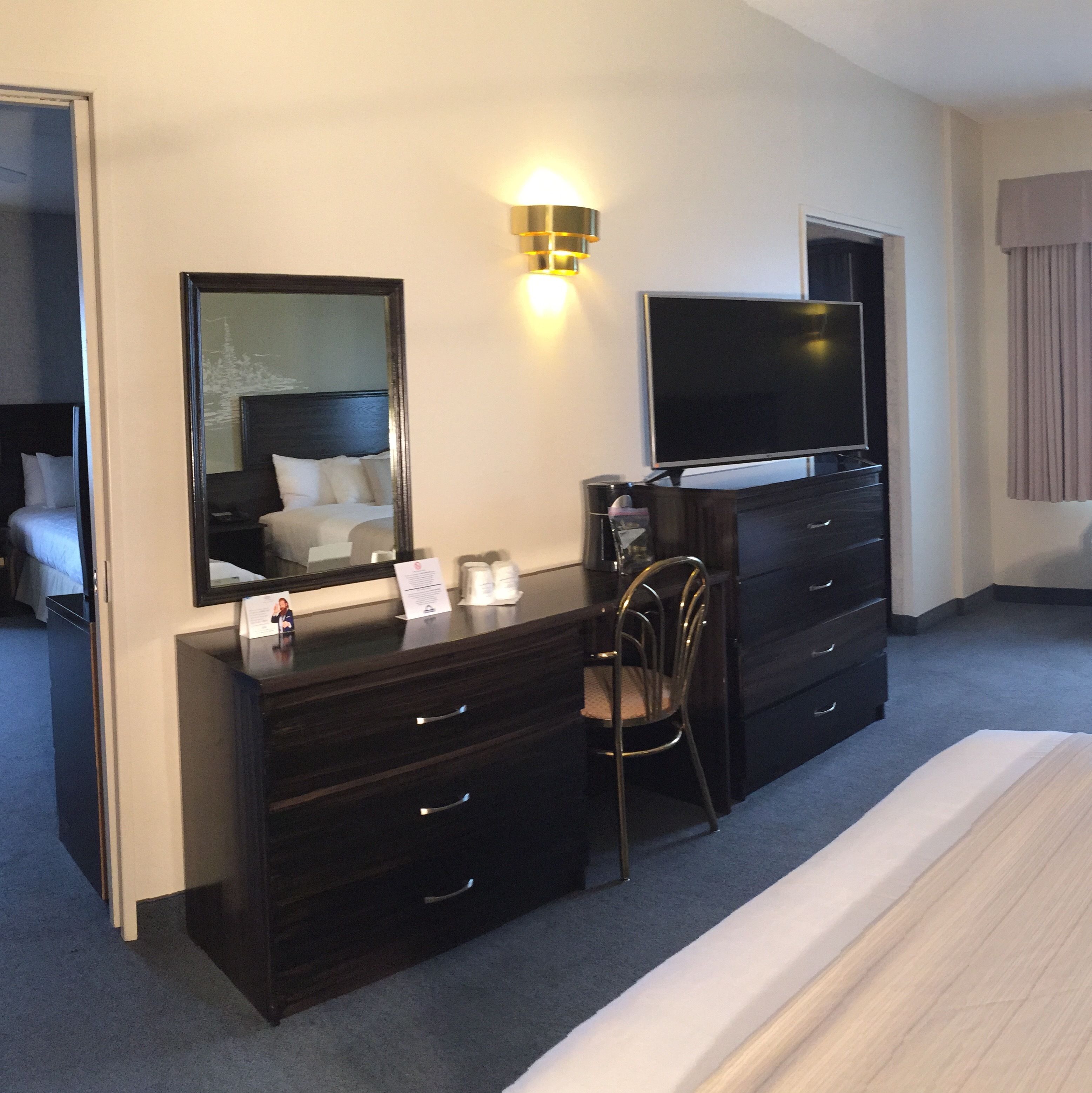 Une chambre d’hôtel avec un lit, une commode, une chaise, un téléviseur et un miroir.