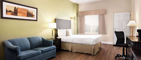 A hotel room with a bed, a blue sofa, a desk, and a framed picture on the wall.
