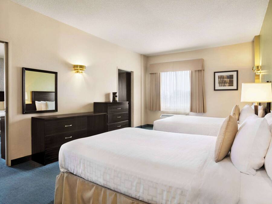 A hotel room with two beds, a dresser, a mirror, and a window with curtains.
