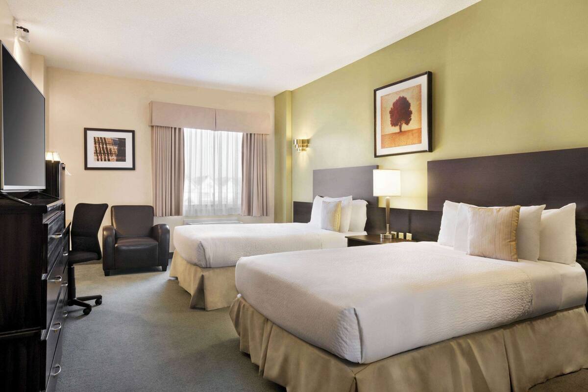 Ein Hotelzimmer mit zwei Betten, einem Schreibtisch, einem Stuhl, einem Fernseher und einem Fenster mit Vorhängen.