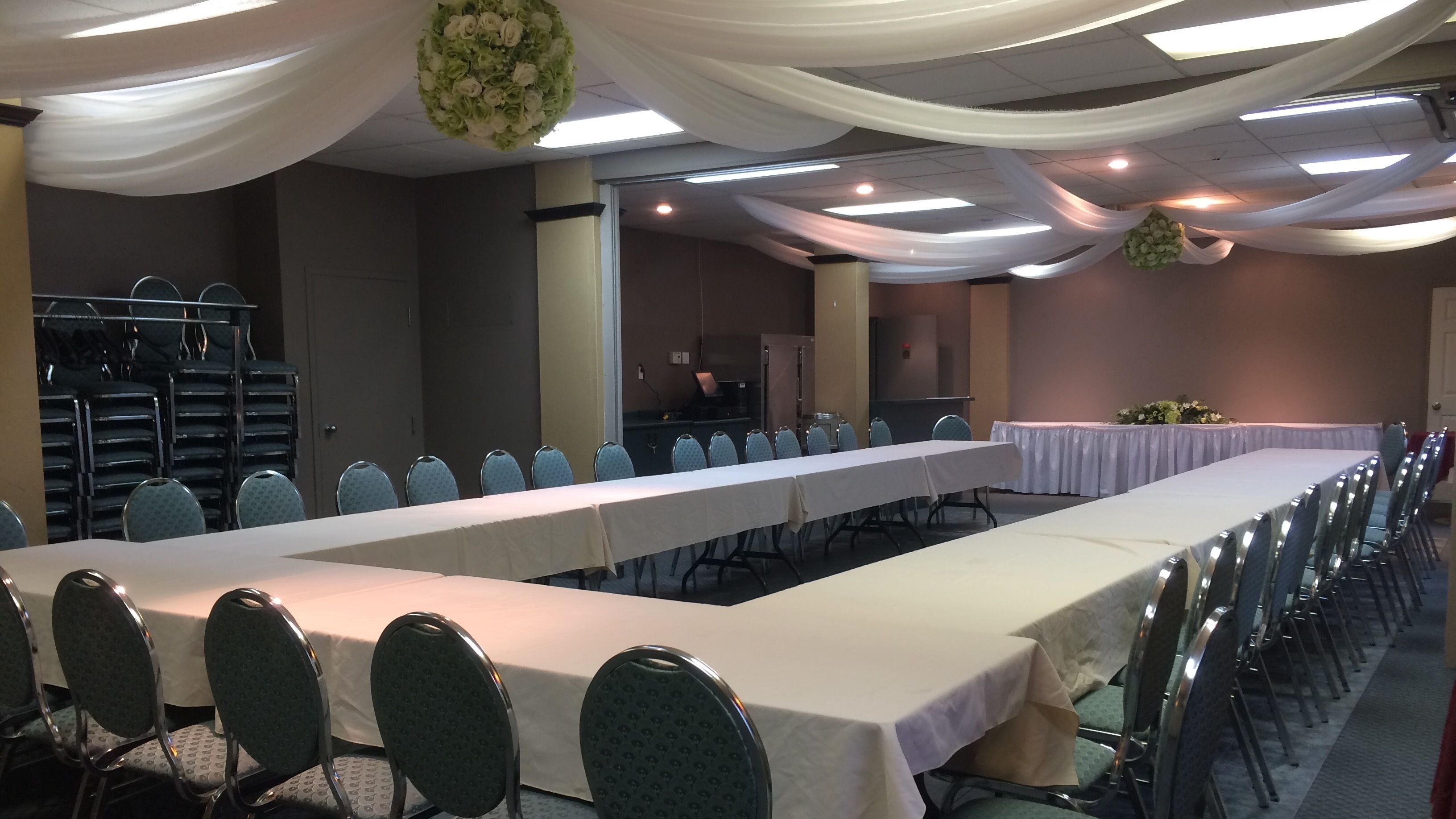 A conference room with long tables and chairs, white drapes, and a chandelier.