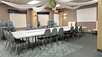 Un salón de conferencias con una larga mesa, sillas, una pizarra y cortinas con drapeado.