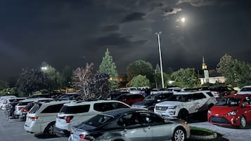 Un estacionamiento de noche con varios autos y un edificio con una torre al fondo.