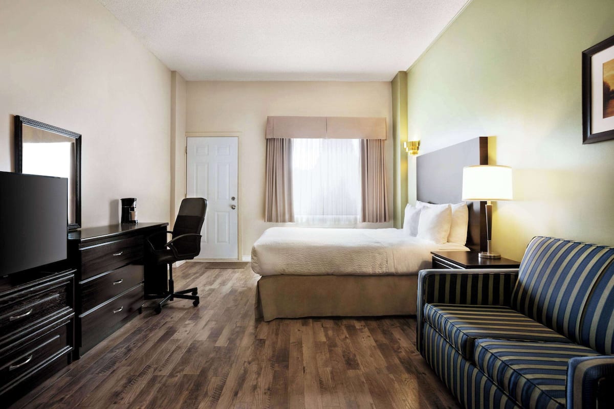 Ein Hotelzimmer mit Bett, Fernseher, Schreibtisch mit Schubladen, Stuhl, Sofa und Lampe.