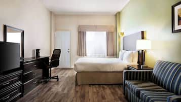 Une chambre d’hôtel comprenant un lit, une télévision, un bureau avec des tiroirs, une chaise, un canapé et une lampe.
