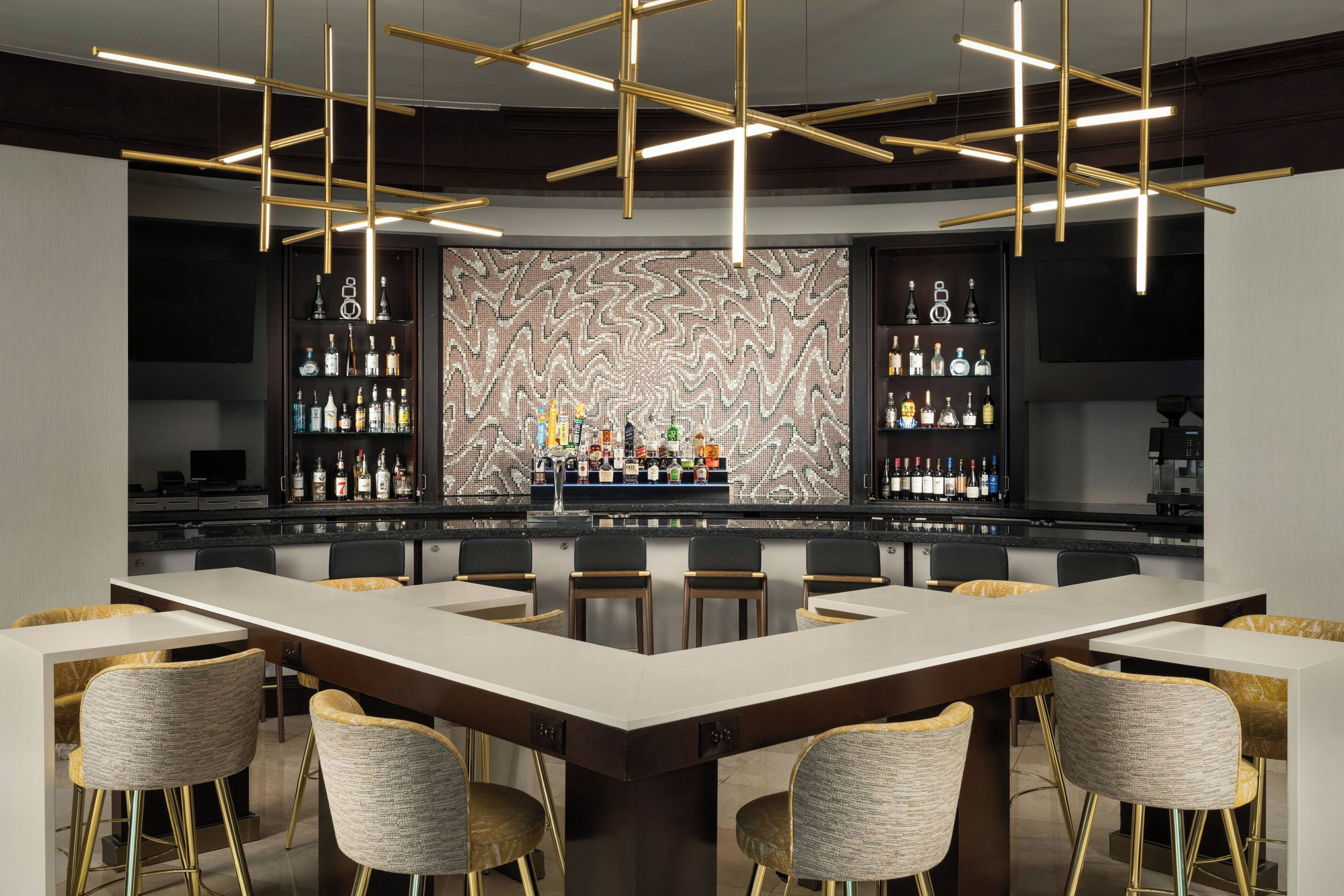 A bar area with a central bar counter, multiple seating options, and a decorative wall with a mosaic pattern.