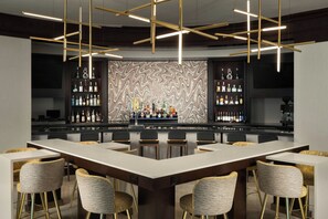 A bar area with a central bar counter, multiple seating options, and a decorative wall with a mosaic pattern. - Renaissance Fort Lauderdale West Hotel (Plantation)