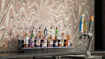 A bar area with a mosaic tile wall, a variety of liquor bottles, and two bar stools.
